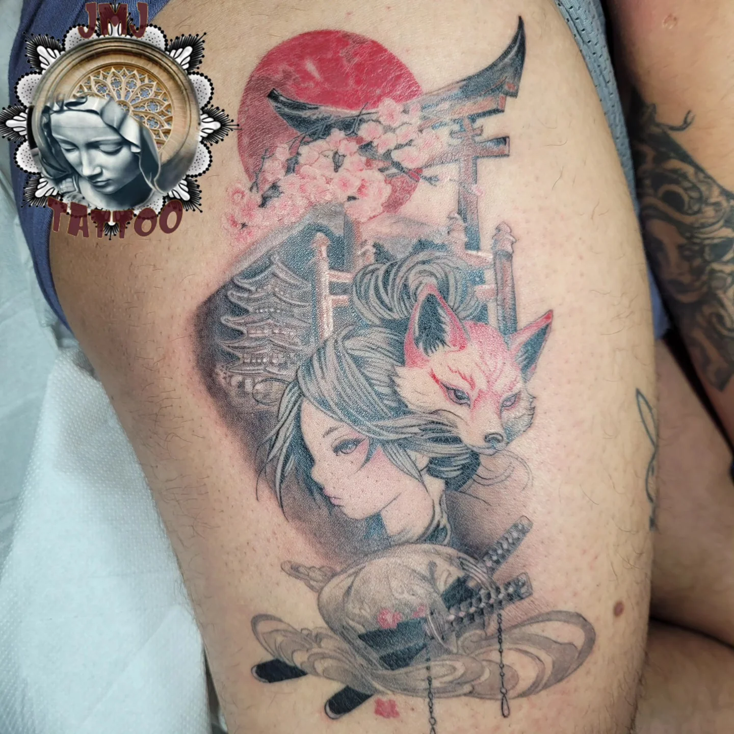 Tatouage japonais sur cuisse représentant une geisha et un masque de renard kitsune sous un torii, avec cerisier en fleur et soleil rouge, réalisé par Jean-Marie Joullié au salon JMJ Tattoo à Sérignan près de Béziers